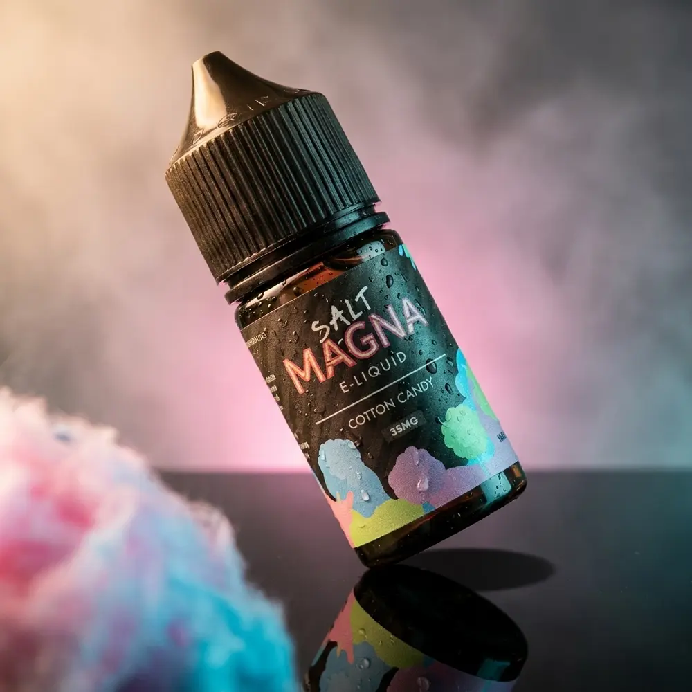 Frasco Magna E-Liquid Salt Cotton Candy em estúdio escuro com reflexo gloss e luzes rosa e ciano - Vapor Gringo