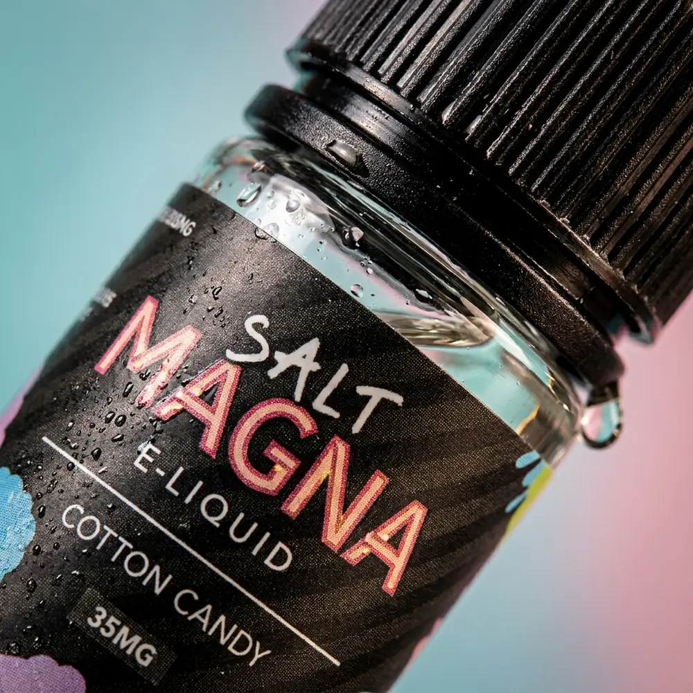 Close-up do rótulo Magna E-Liquid Salt Cotton Candy com gotas de condensação e reflexos na tampa - Vapor Gringo