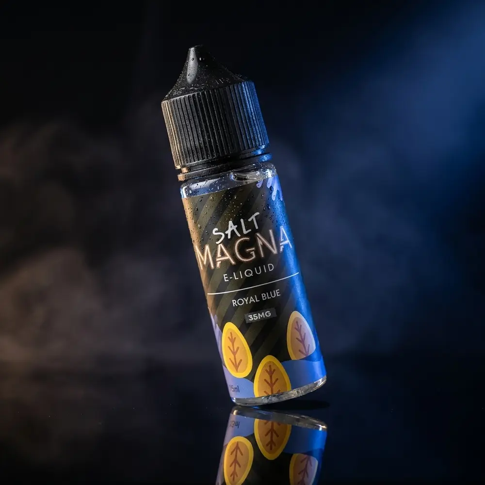 Garrafa do Líquido Magna Royal Blue Tabaco Gelado sobre base preta com iluminação azul e reflexos sofisticados - Vapor Gringo