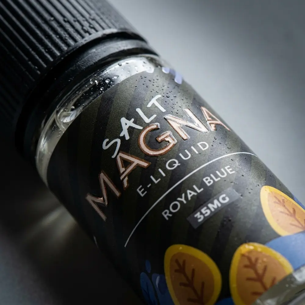 Detalhe do rótulo do Líquido Magna Royal Blue Tabaco Gelado mostrando textura, gotas e reflexos no bocal - Vapor Gringo