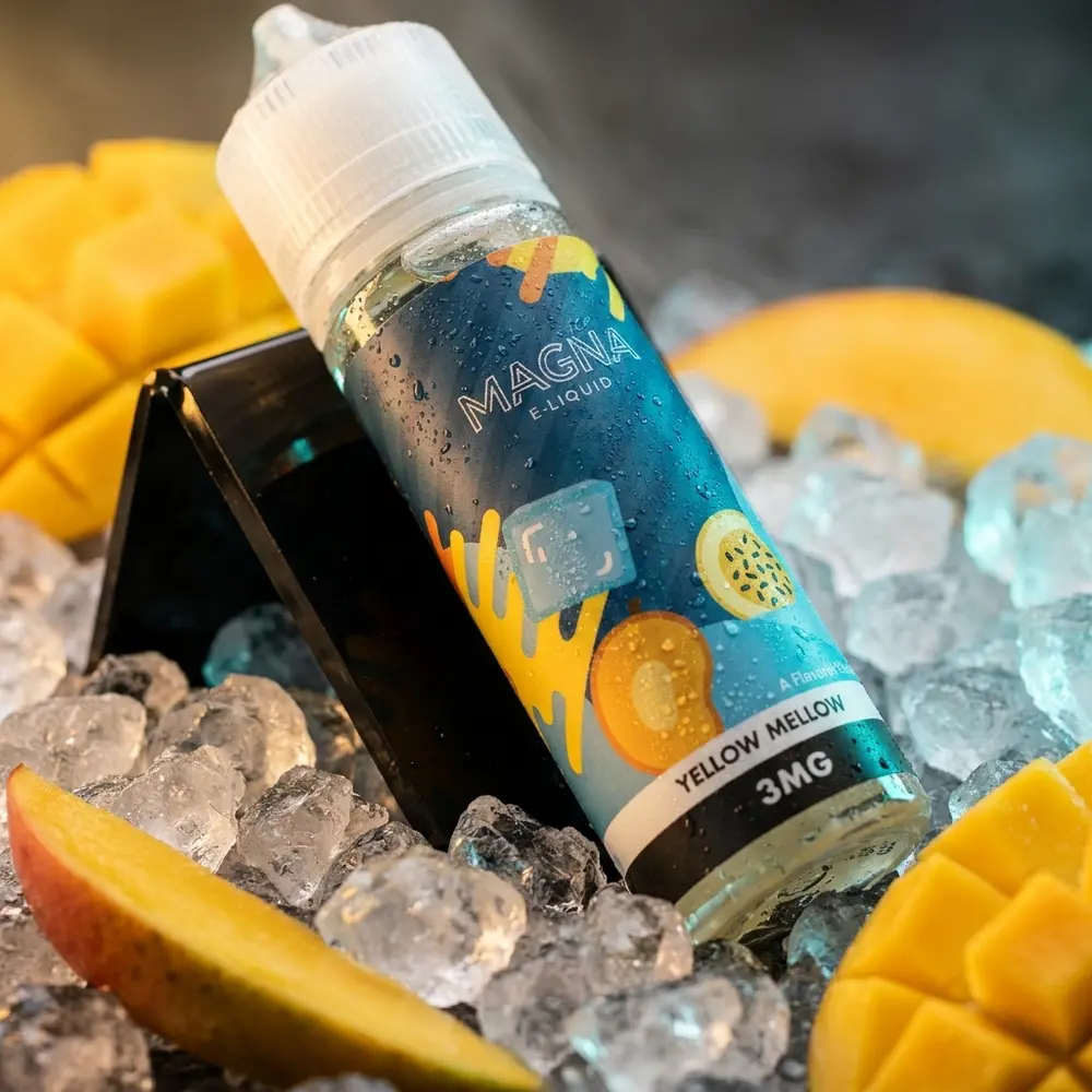 Frasco do Líquido Magna Yellow Melow Ice sobre base acrílica com gelo, fatias de manga e iluminação amarela e azul - Vapor Gringo