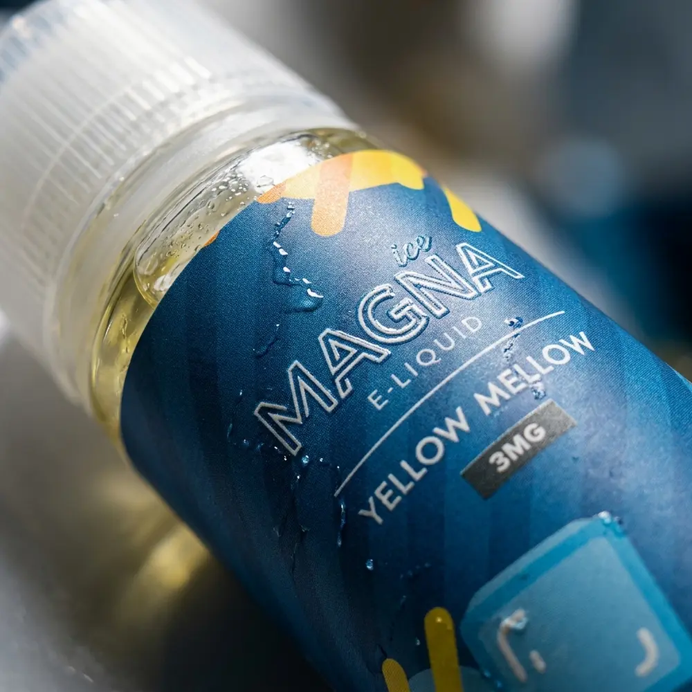 Close-up do rótulo e bico do Líquido Magna Yellow Melow Ice com gotas de condensação e reflexos metálicos - Vapor Gringo