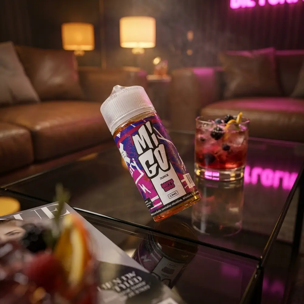 frasco de 100ml do liquido migo - berry good apoiado em mesa de lounge com coquetel de frutas e luzes ambar e magenta - Vapor Gringo