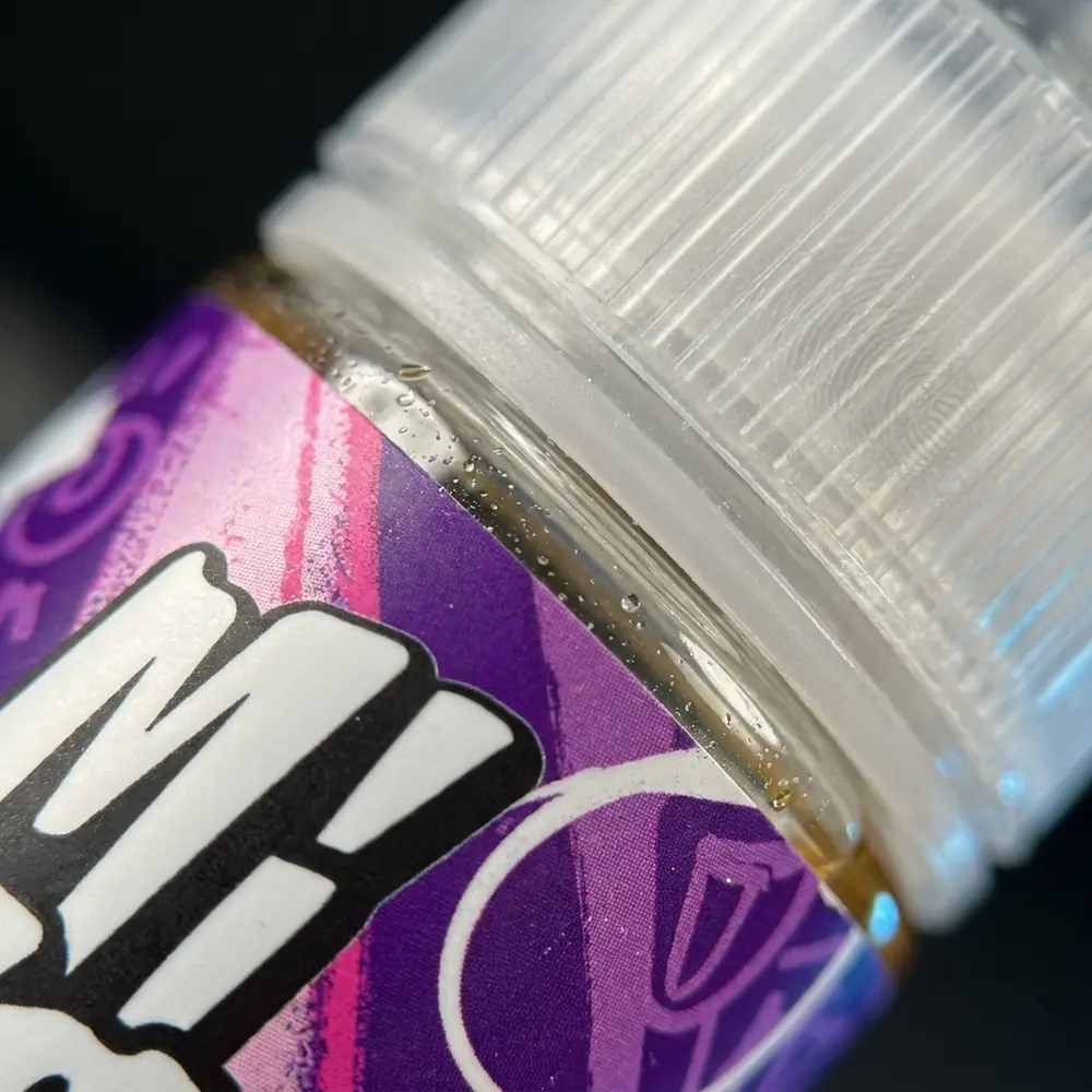 Macro do rótulo e bocal do Líquido Migo - Bubbaloova com gotas de condensação e reflexos metálicos detalhados - Vapor Gringo