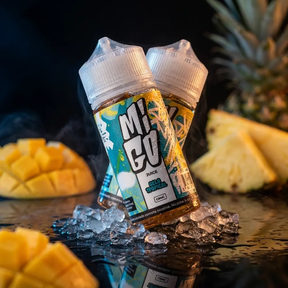 Frasco Líquido Migo Gelo Tropical inclinado sobre acrílico preto com gelo e fatias de frutas tropicais desfocadas - Vapor Gringo
