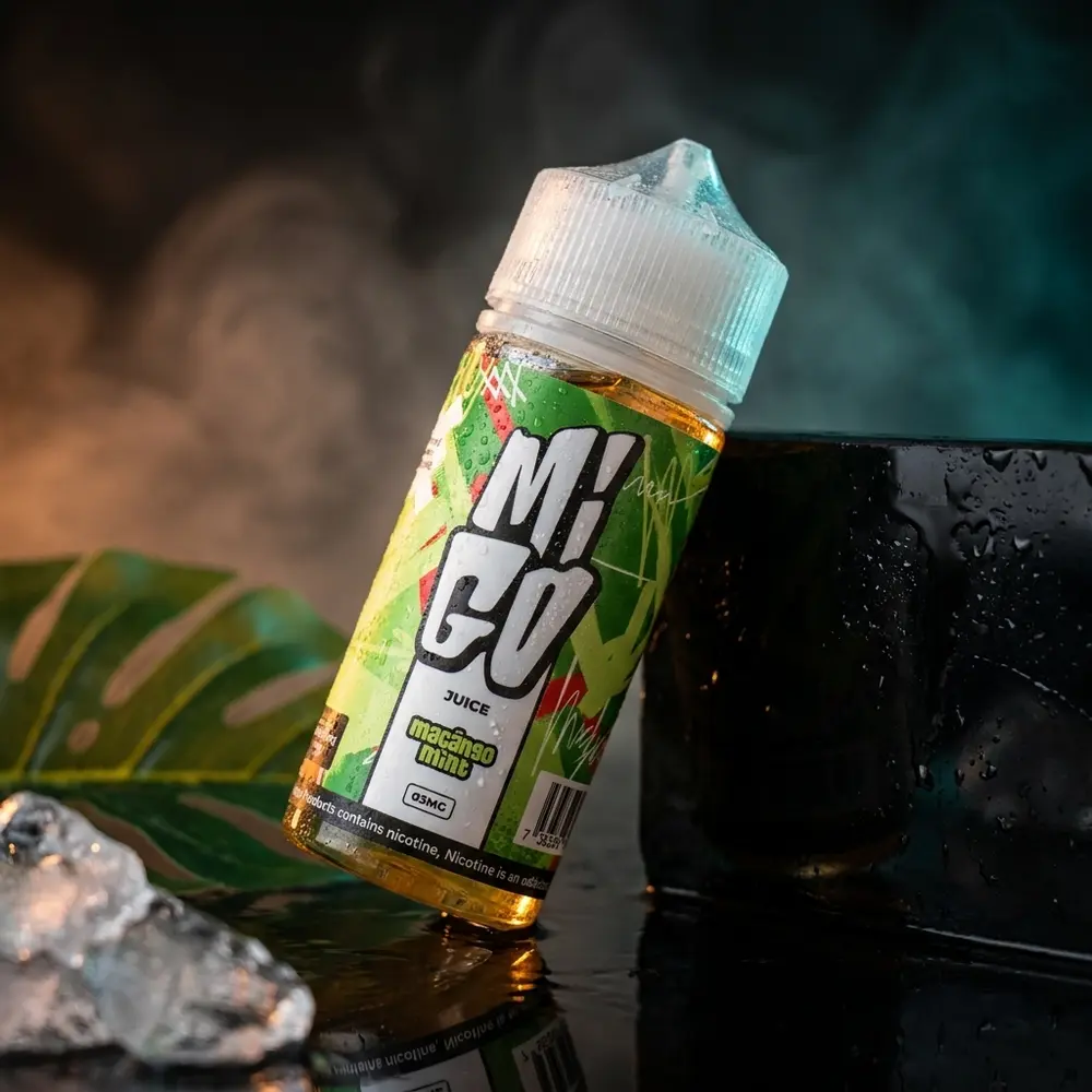 Garrafa Líquido Migo Maçãngo Mint 100ml sobre base preta molhada com condensação e luzes âmbar e turquesa - Vapor Gringo