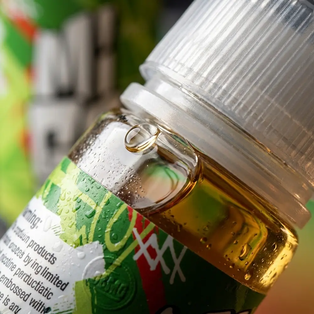 Close-up do rótulo e bico do Líquido Migo Maçãngo Mint 100ml com gotas de condensação e reflexos no vidro - Vapor Gringo