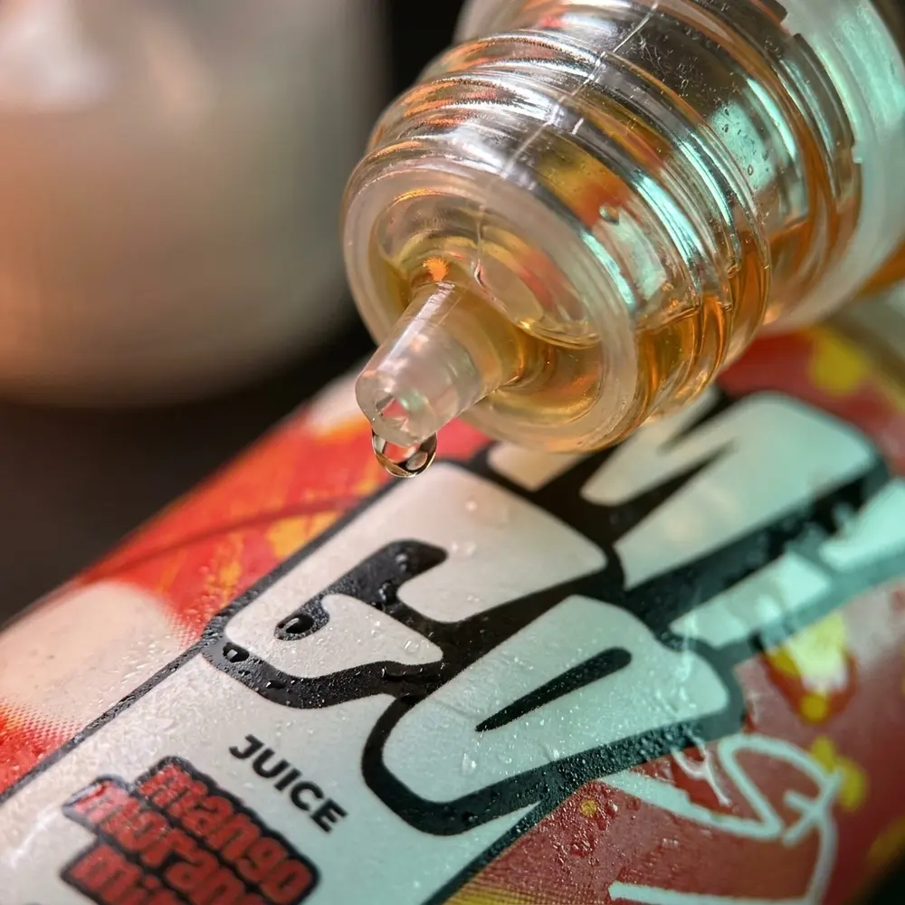 Close-up do rotulo do Liquido Migo Mango Morango Mint com gotas, textura do vidro e detalhe do bico - Vapor Gringo