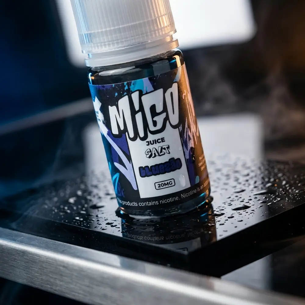 Frasco do Líquido Migo Salt Bluezão sobre base acrílica molhada, reflexos azuis e detalhes metálicos - Vapor Gringo