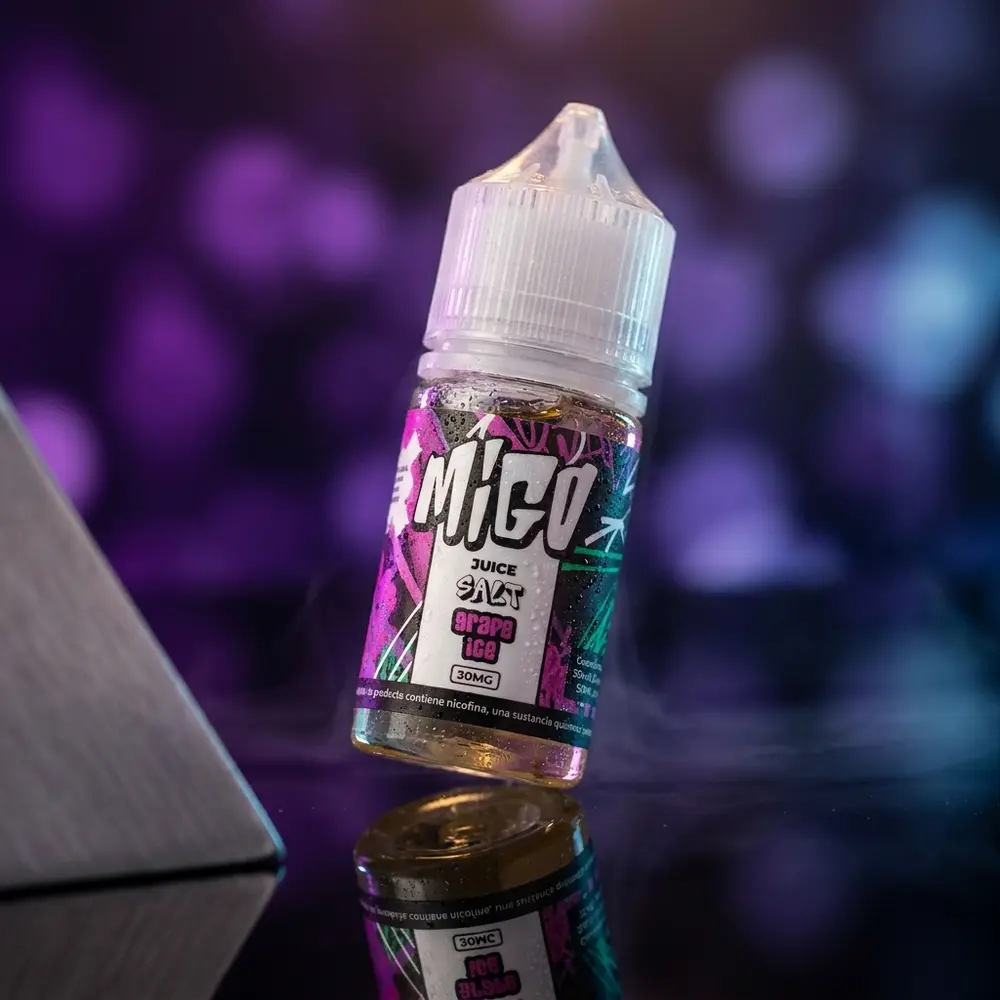 Frasco Líquido Migo Salt Grape Ice 30ml inclinado sobre superfície preta brilhante, gotas de condensação e luzes roxas e azuis. - Vapor Gringo