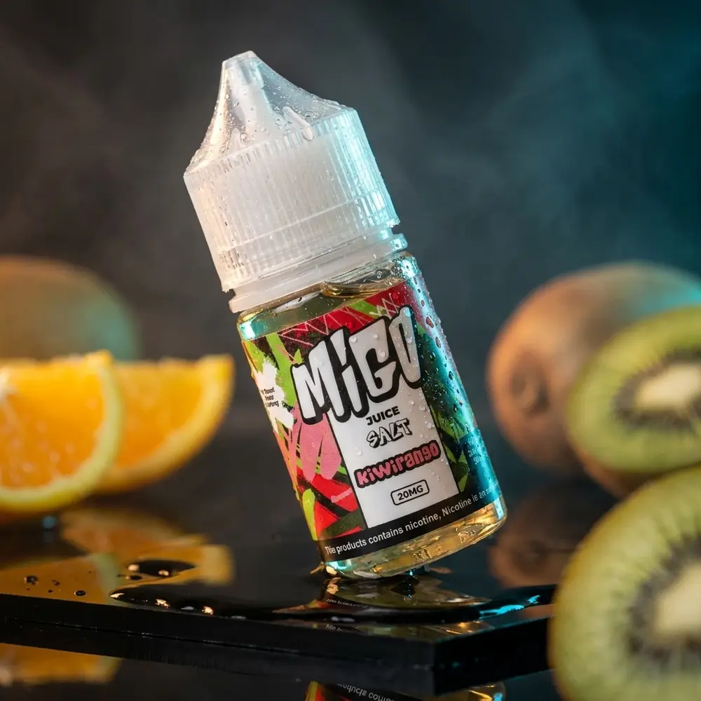 Frasco do Líquido Migo Salt Kiwirango sobre acrílico preto molhado, gotas e fatias de kiwi e laranja desfocadas - Vapor Gringo