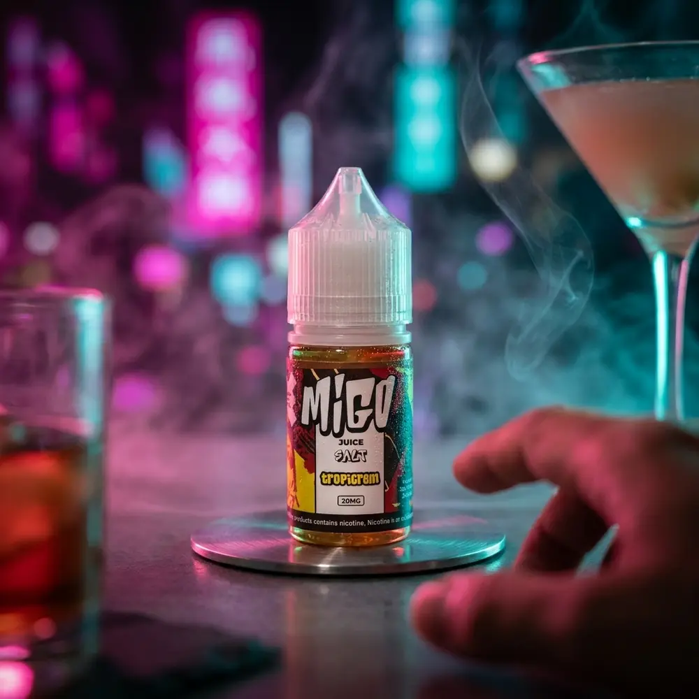 Líquido Migo Salt Tropicrem apoiado em coaster metálico num lounge urbano neon, copo e mão desfocados - Vapor Gringo
