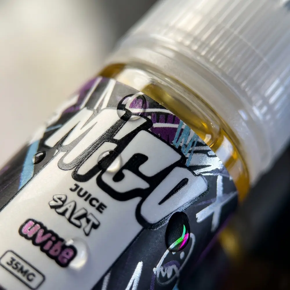 Macro do rótulo e tampa do Líquido Migo Salt - Uvibe com gotas de condensação e reflexos nítidos - Vapor Gringo