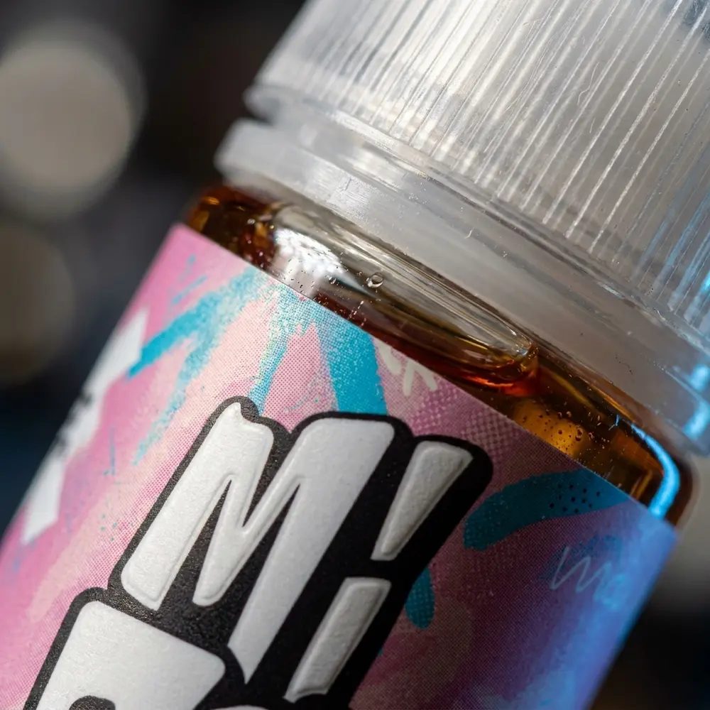 Close-up do rótulo e bico da garrafa Líquido Migo Sweet Nuvem com gotículas, textura do rótulo e reflexos - Vapor Gringo