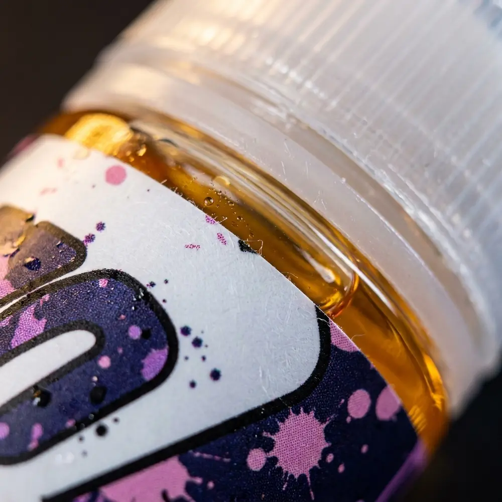 Detalhe macro do rótulo e bocal do Líquido Migo Uvaloo com gotículas e micro-reflexos - Vapor Gringo