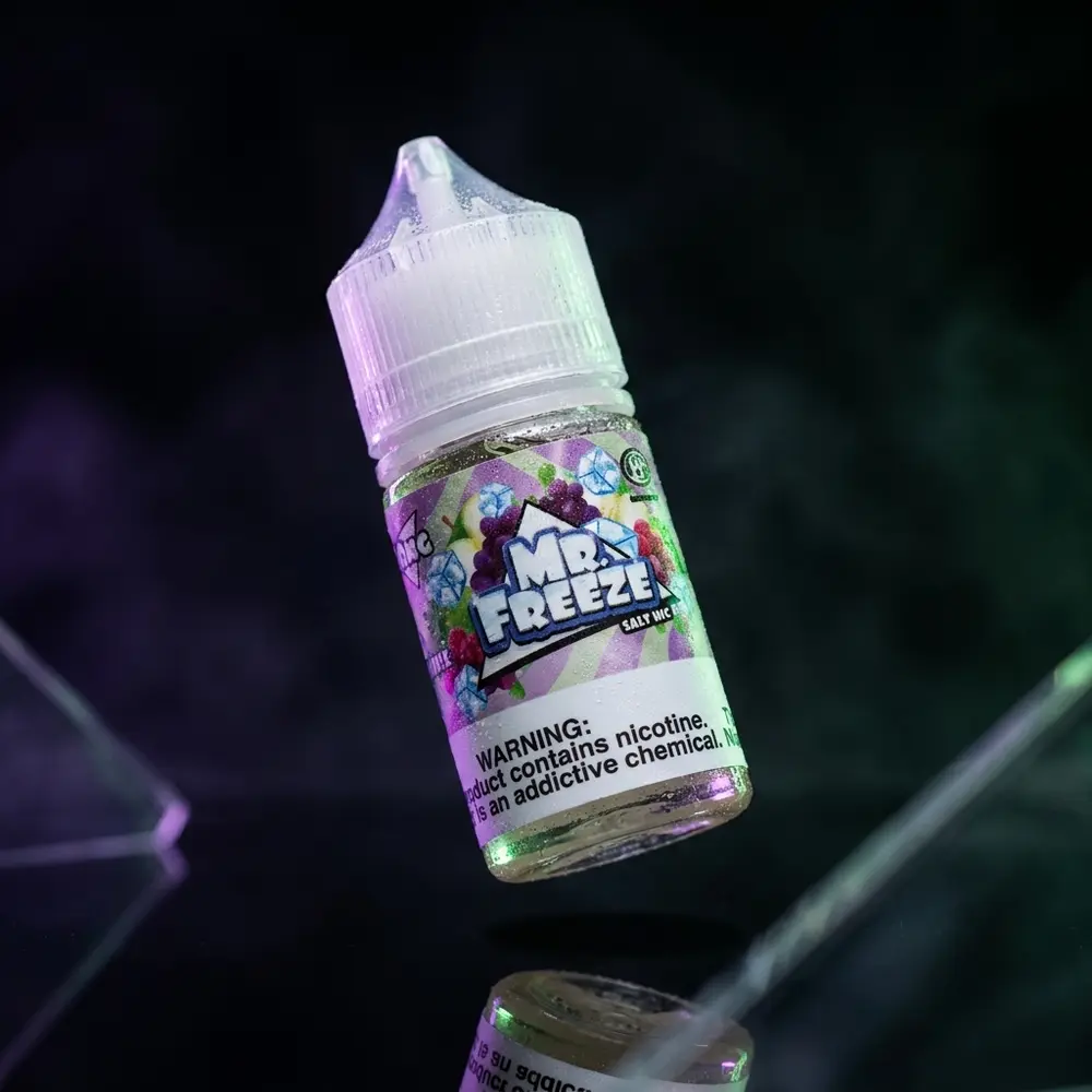 Garrafa Liquido Mr. Freeze Salt Grape Green Apple Frost inclinada sobre acrilico preto com gotas e luzes roxa e verde - Vapor Gringo