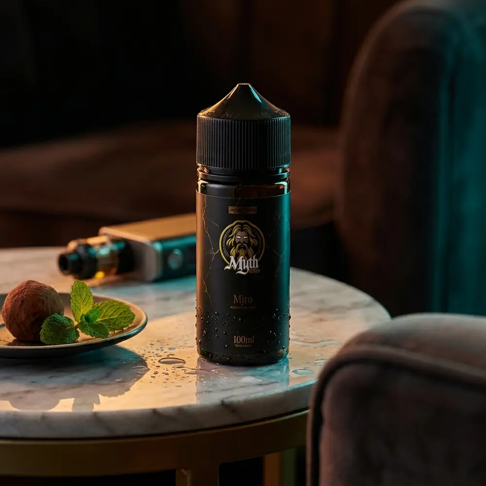 Frasco do Líquido Myth Hera 100ml Chocolate Mint em mesa de mármore de lounge escuro com trufa e folha de menta. - Vapor Gringo