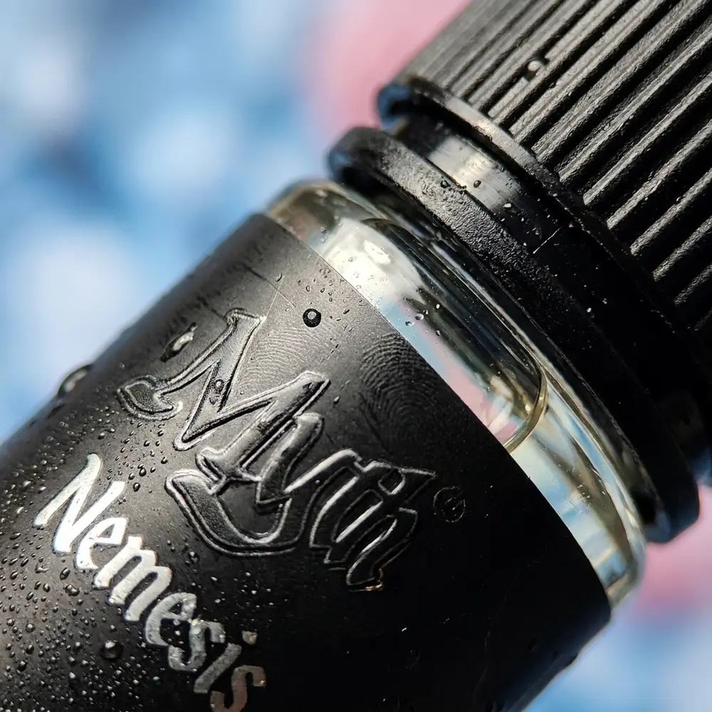 Close-up do rótulo e bico do Líquido Myth Salt Nemesis Lychee Ice, gotas, textura do plástico e reflexos metálicos - Vapor Gringo