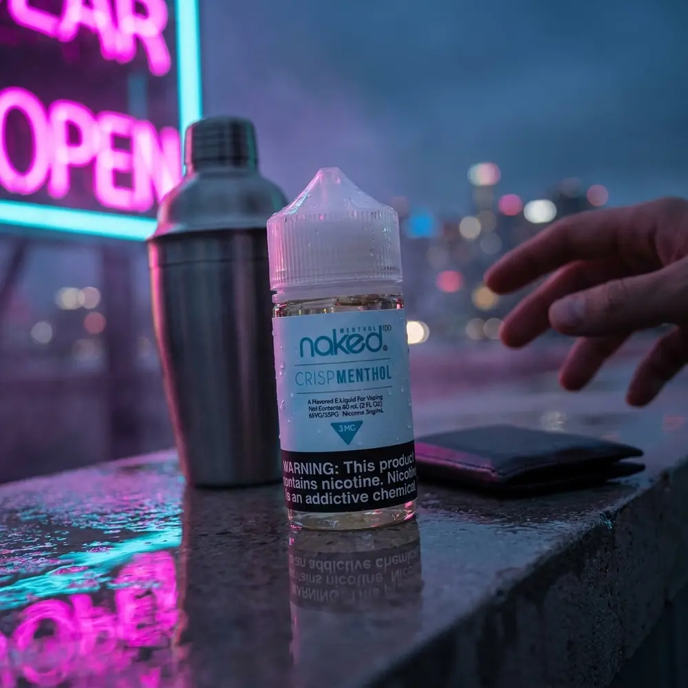 Frasco Naked 100 Crisp Menthol apoiado em borda molhada de bar urbano com reflexos neon ao fundo - Vapor Gringo