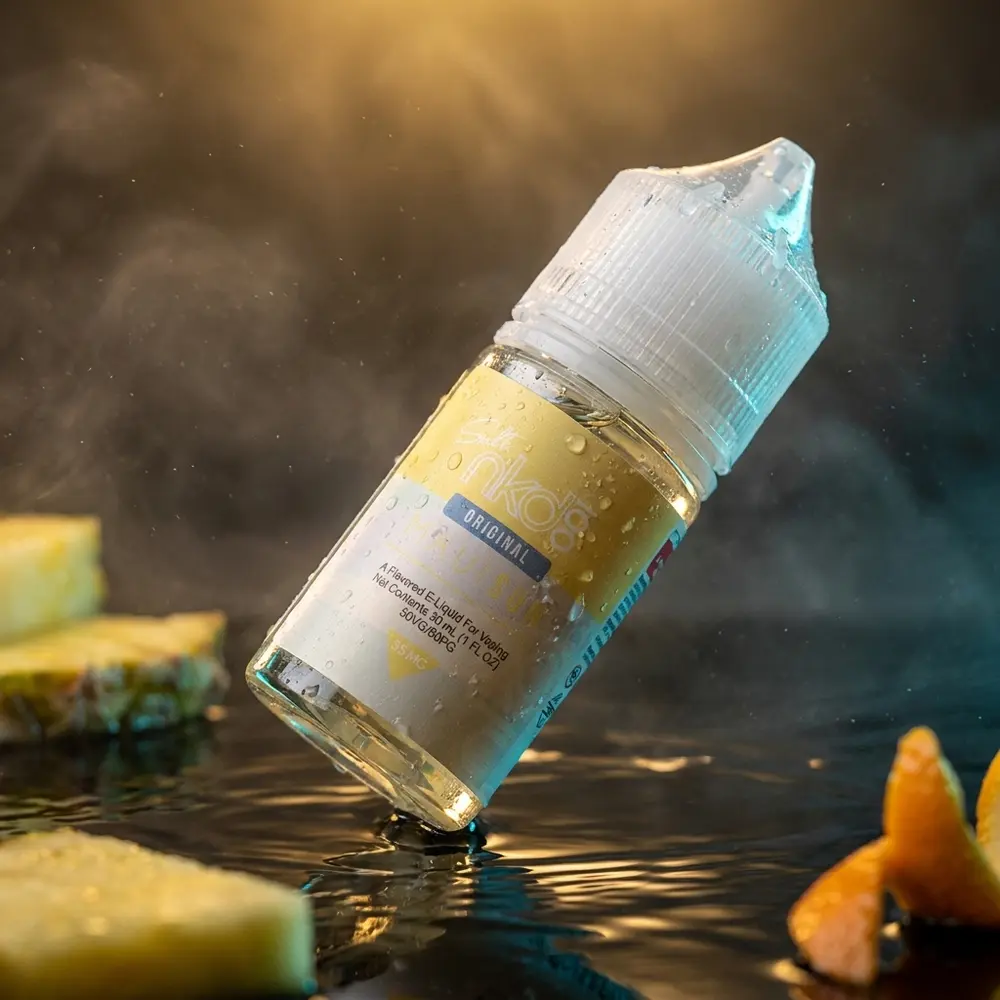 Frasco de líquido Naked 100 Salt Maui Sun sobre acrílico preto molhado com reflexos tropicais e névoa sutil. - Vapor Gringo