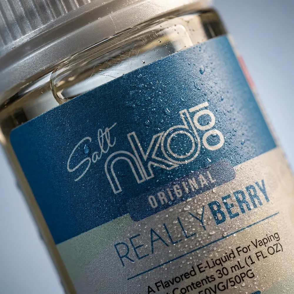 Detalhe macro do rótulo Naked 100 Salt Really Berry mostrando tipografia, textura do vidro e gotas de condensação - Vapor Gringo