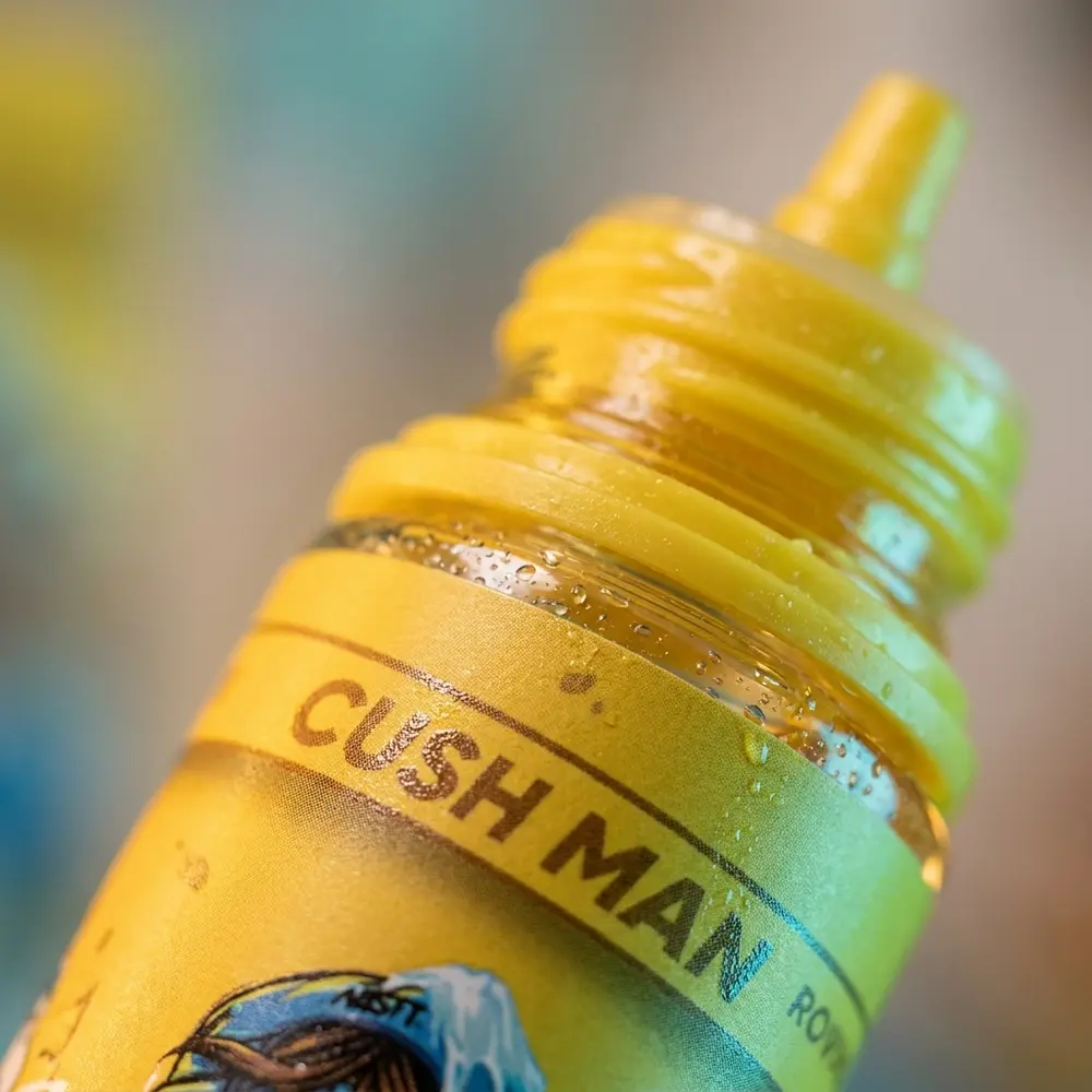 Detalhe do bico, rosca e etiqueta da Nasty Juice Cush Man Mango Banana com gotas de condensação e textura do rótulo - Vapor Gringo