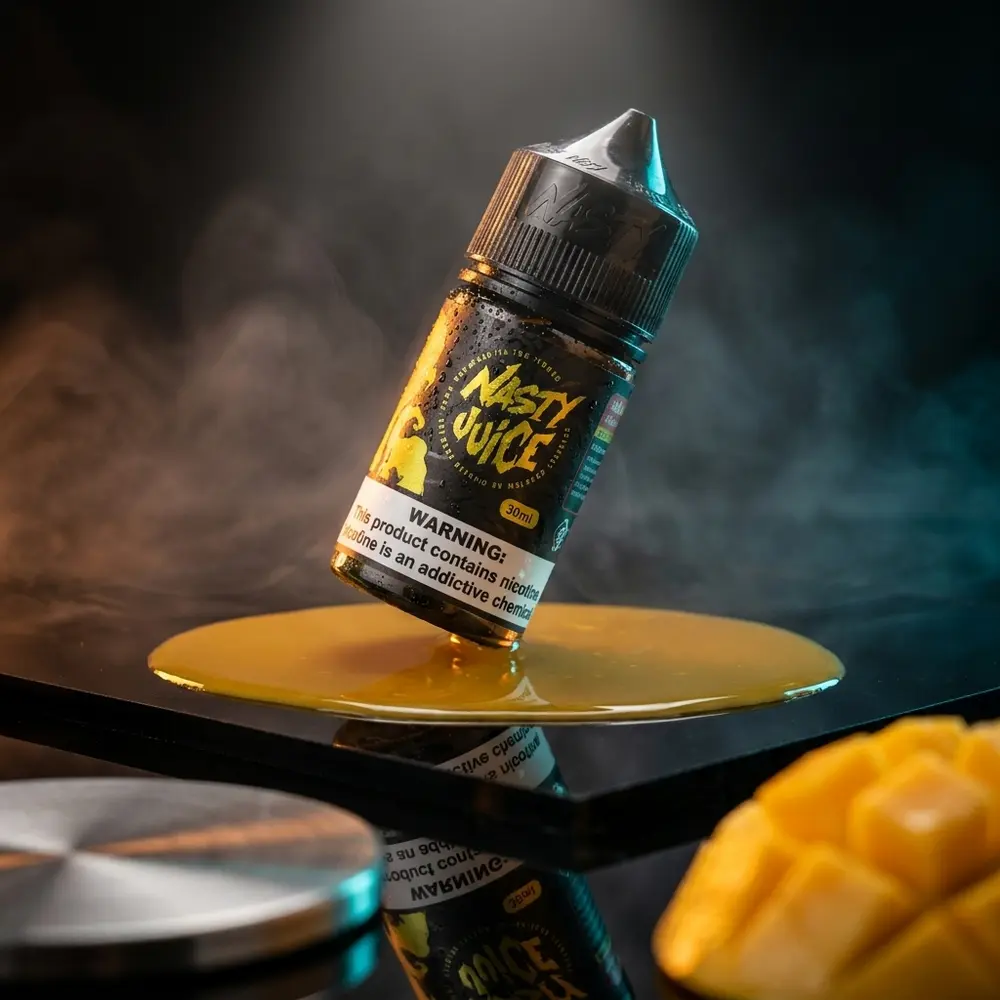 Garrafa do Líquido Nasty Juice Salt Mango Lassi sobre acrílico escuro, iluminação laranja e ciano, gotas e reflexos nítidos - Vapor Gringo