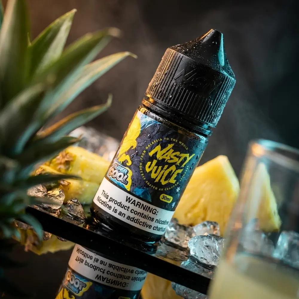 Frasco Nasty Juice Pineapple Ice sobre acrílico preto com fatias de abacaxi e gelo, luzes âmbar e azul - Vapor Gringo