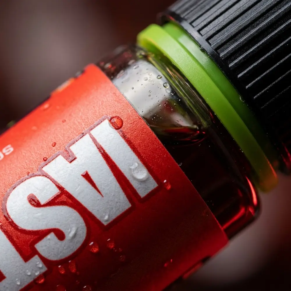 Close-up do rotulo e bico do Liquido Nasty Juice Salt Cherry Cola com condensacao e reflexos microdetalhados - Vapor Gringo