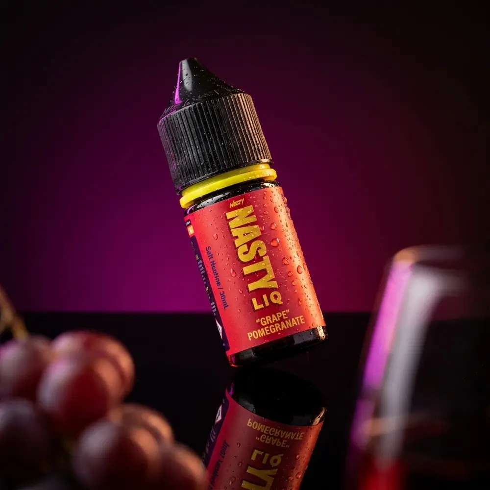 Frasco do Líquido Nasty Juice Salt Grape Pomegranate sobre base preta brilhante com gotas e reflexos marcantes - Vapor Gringo