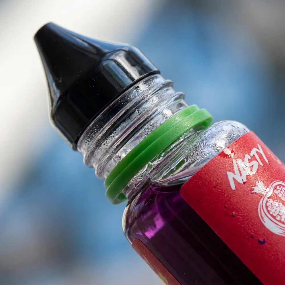 Close-up do bocal e rótulo do Líquido Nasty Juice Salt Grape Pomegranate com gotas e textura impressa visíveis - Vapor Gringo