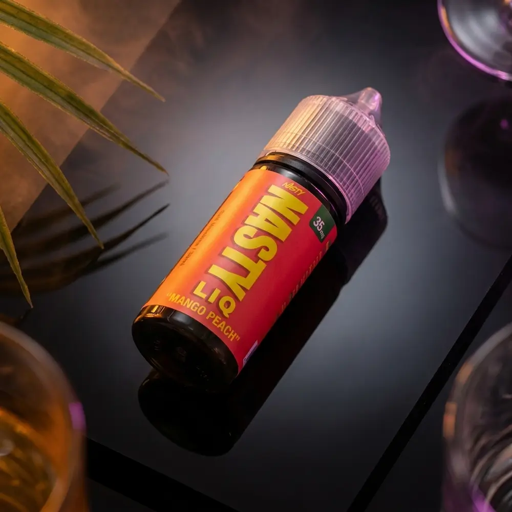 Frasco Nasty Juice Salt Mango Peach sobre base acrílica preta reflexiva com luzes quentes laranja e pêssego - Vapor Gringo