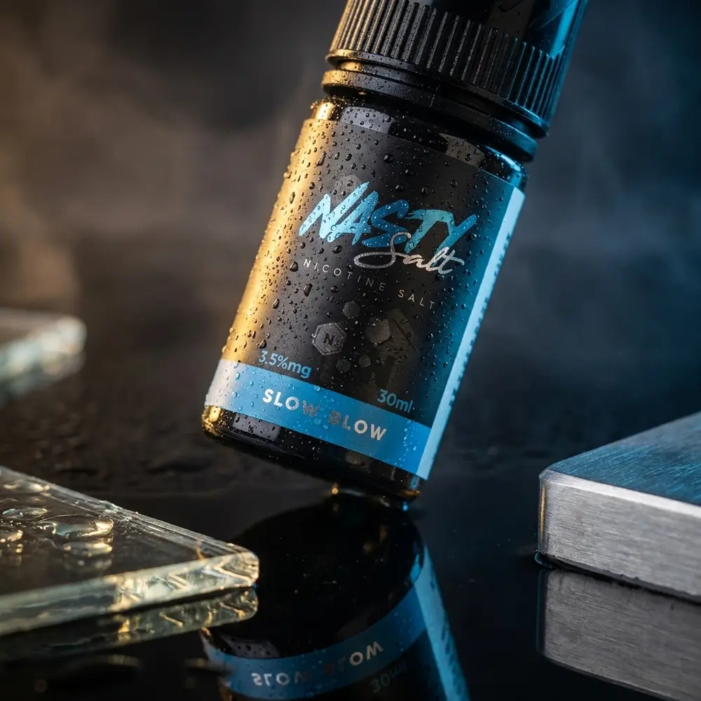 Garrafa Nasty Juice Salt Slow Blow inclinada sobre acrilico preto molhado, rótulo intacto e gotas de condensação - Vapor Gringo