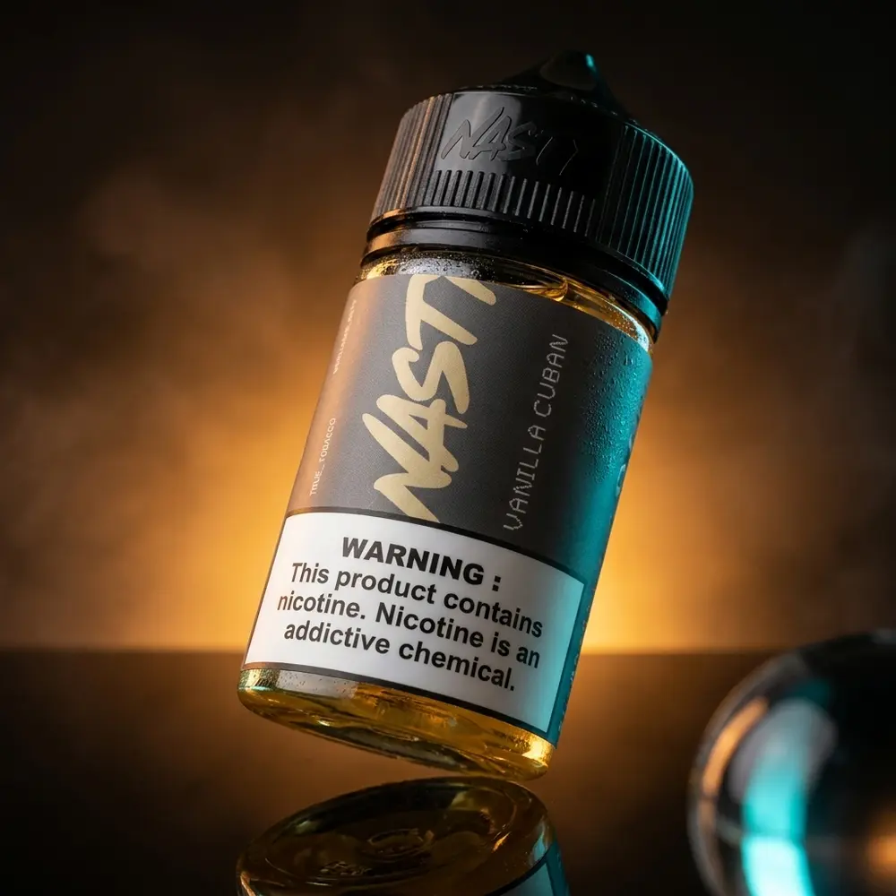 Garrafa Liquido Nasty Juice Salt Vanilla Cuban 30ml inclinada sobre base preta refletiva, rótulo visível e iluminação âmbar e ciano - Vapor Gringo