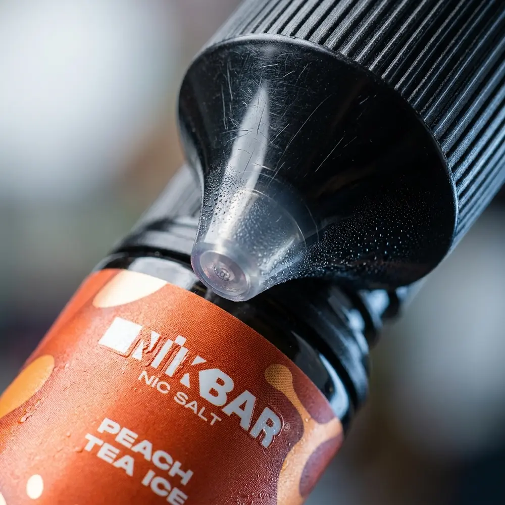 Close extremo do frasco Nikbar Salt Peach Tea Ice mostrando fecho, rotulo e gotas de condensacao com textura visivel - Vapor Gringo