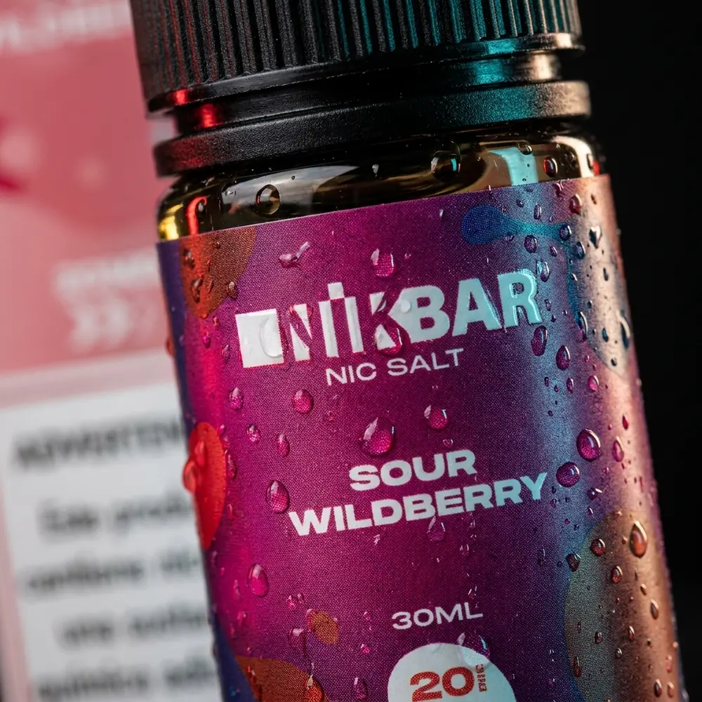 Close-up do rótulo e bico da garrafa Nikbar Salt Sour Wildberry 30ml com gotas, textura e microreflexos - Vapor Gringo