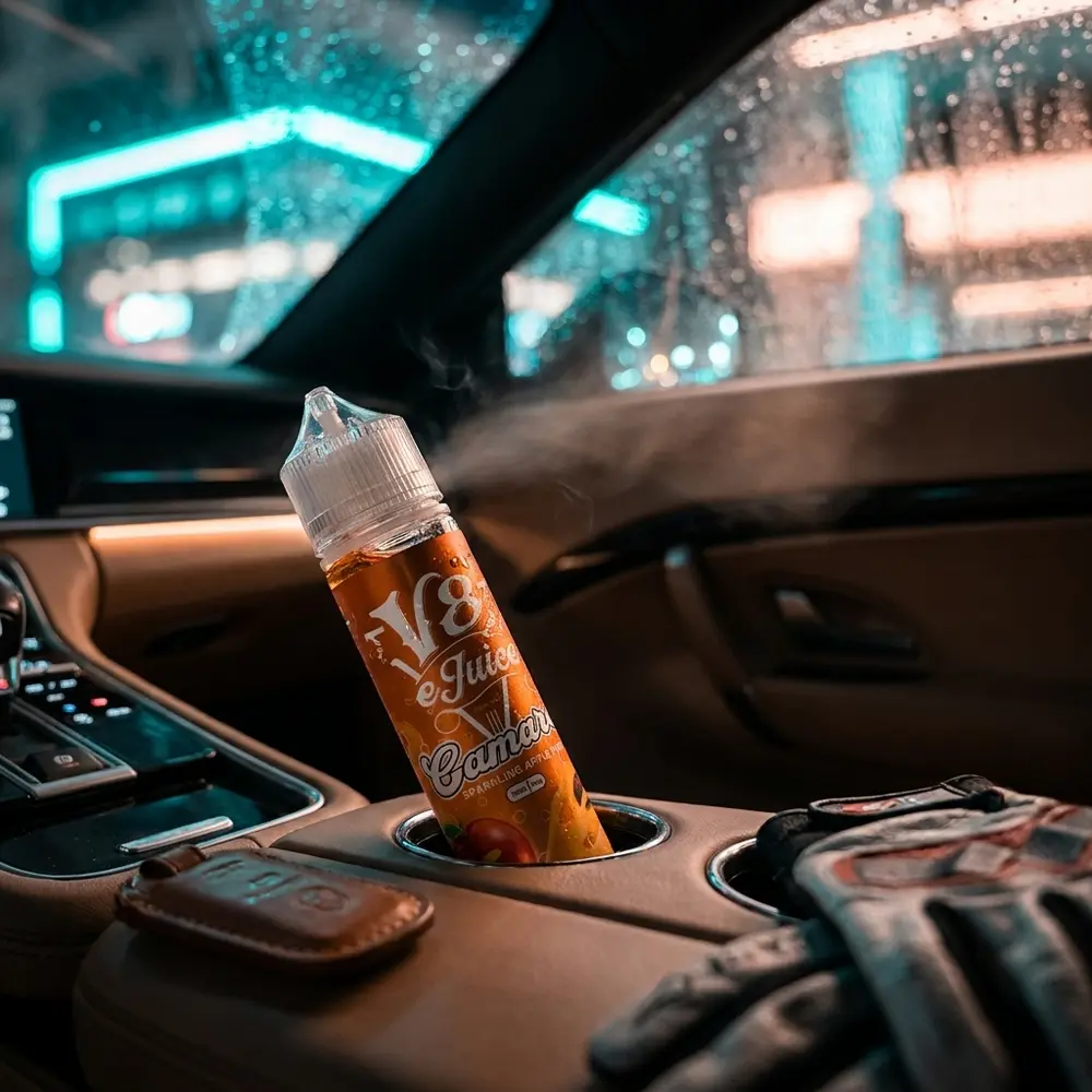 Frasco Líquido V8 E-Juice Camaro apoiado no console de um carro premium, luzes urbanas desfocadas ao fundo - Vapor Gringo