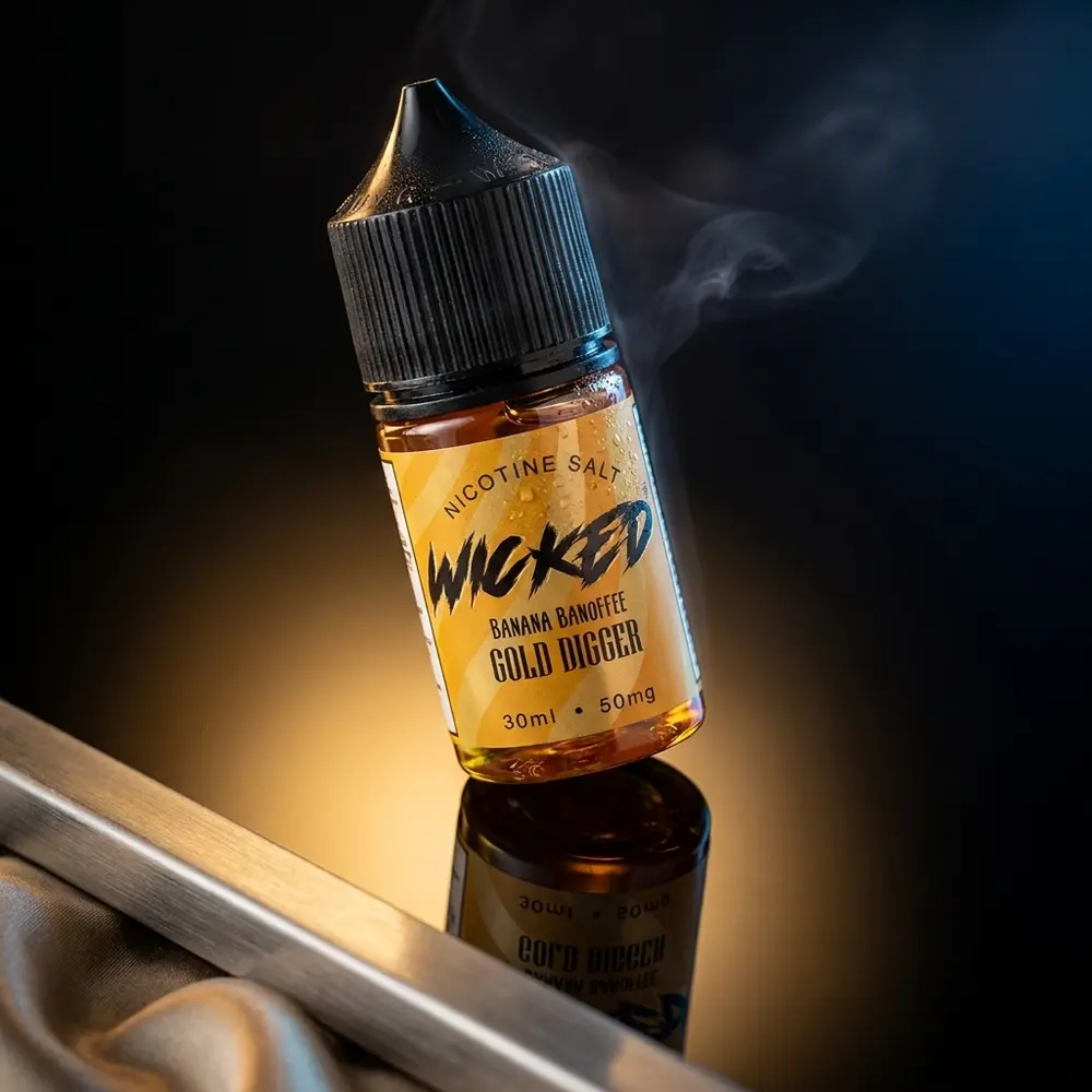 Garrafa Wicked Salt Banana Banoffee Gold Digger inclinada sobre acrilico preto, reflexos dourados e gotas de condensacao - Vapor Gringo