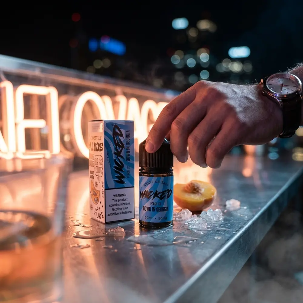 Frasco Wicked Salt Peach Ice no balcão molhado de bar urbano com néon pêssego e luzes da cidade ao fundo. - Vapor Gringo