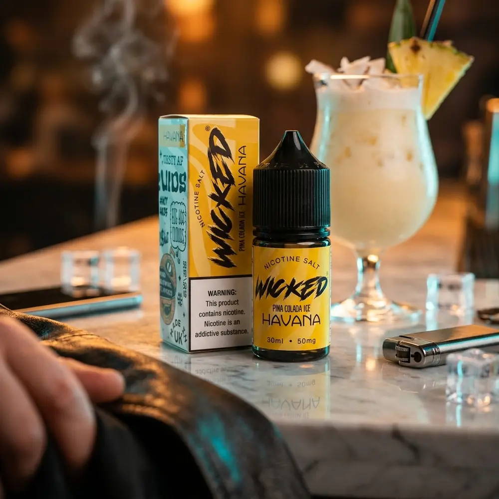 Líquido Wicked Salt Pina Colada Ice Havana no balcão de lounge luxuoso junto a coquetel e mão desfocada - Vapor Gringo