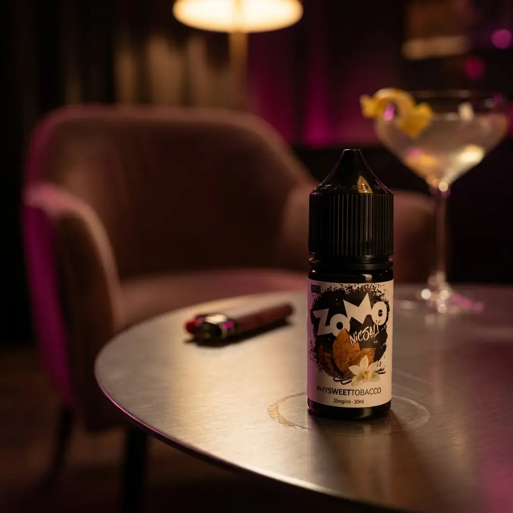 Garrafa Zomo Salt Sweet Tobacco 30ml em lounge urbano sobre mesa metálica, luzes quentes e objetos de lifestyle ao fundo - Vapor Gringo