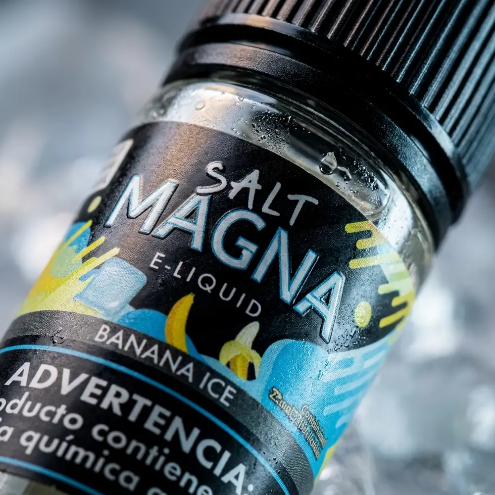 Detalhe macro do rotulo e bico da Magna Banana Ice 30ml com gotas, textura do vidro e reflexos metalicos - Vapor Gringo