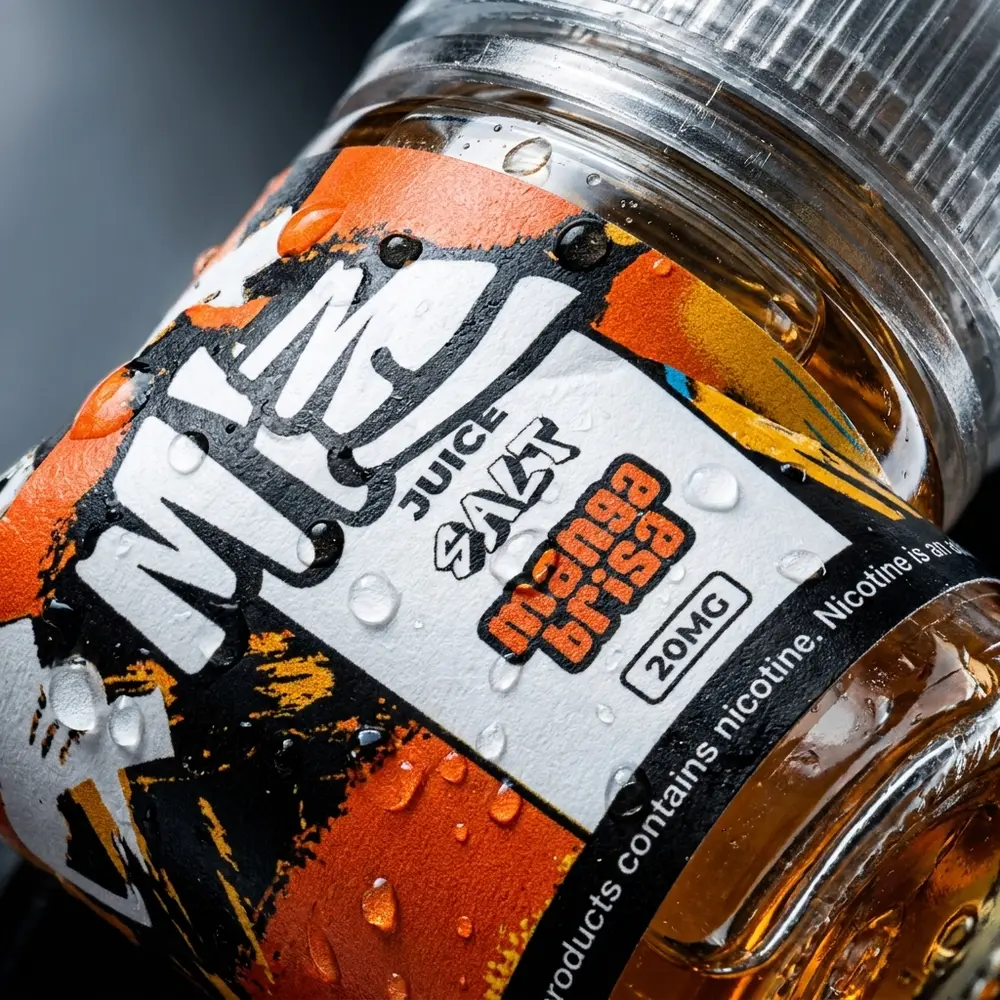 Close-up do rótulo e bico do Migo Salt Mangabrisa 30ml com gotas de condensacao e reflexos meticulosamente reais - Vapor Gringo