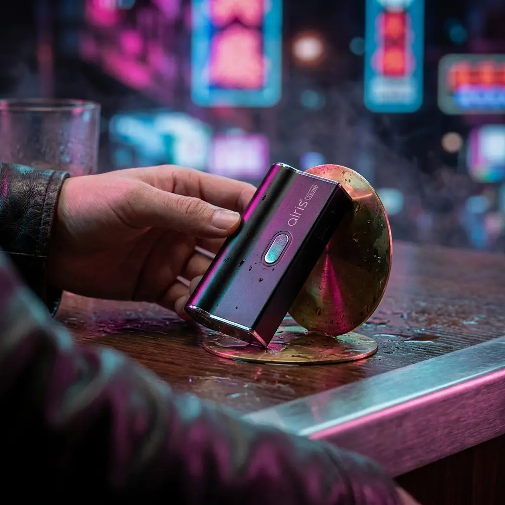 Mod AIRIS Janus 2in1 apoiado em balcão molhado com reflexos neon urbanos e mão parcial ao lado - Vapor Gringo