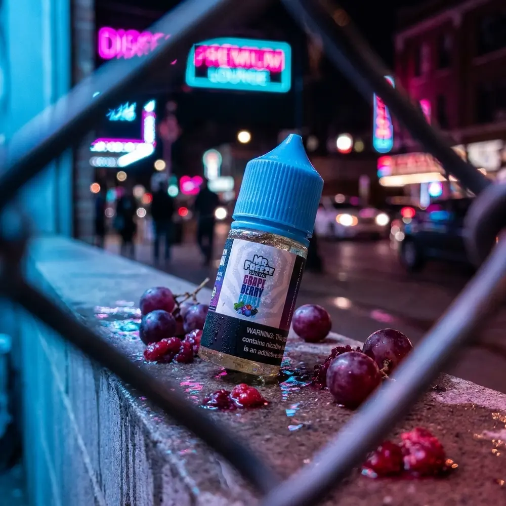 Garrafa Mr. Freeze Salt Grape Berry Frost sobre parapeito molhado com reflexos neon e frutas vermelhas ao redor - Vapor Gringo