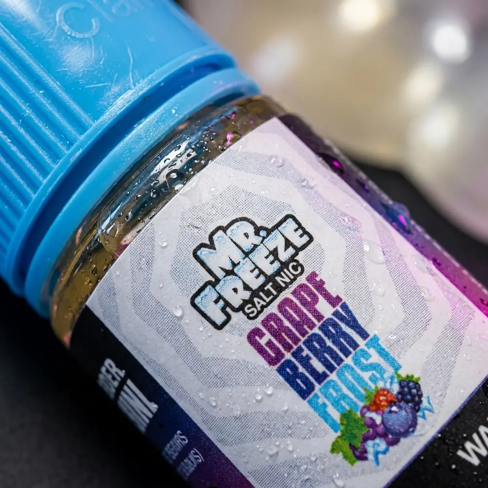 Close-up do rótulo e bico do Mr. Freeze Salt Grape Berry Frost com gotículas de condensação e reflexos coloridos - Vapor Gringo