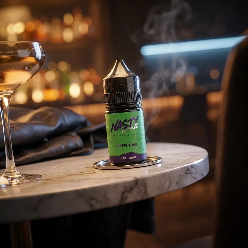 Garrafa Nasty Juice Salt Hippie Trail 30ml em mesa de lounge sofisticado, ao lado de copo e jaqueta de couro. - Vapor Gringo