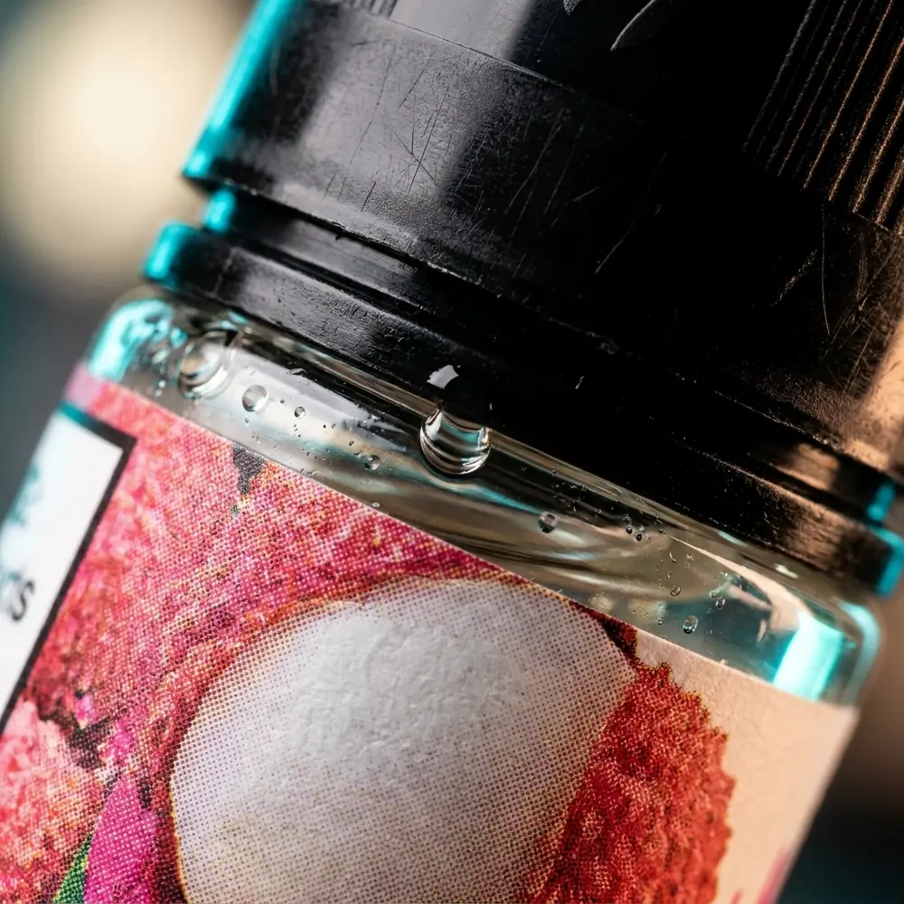 Close da etiqueta e do bico do Nasty Juice Salt Lychee 30ml com gotículas, textura do vidro e reflexos detalhados. - Vapor Gringo