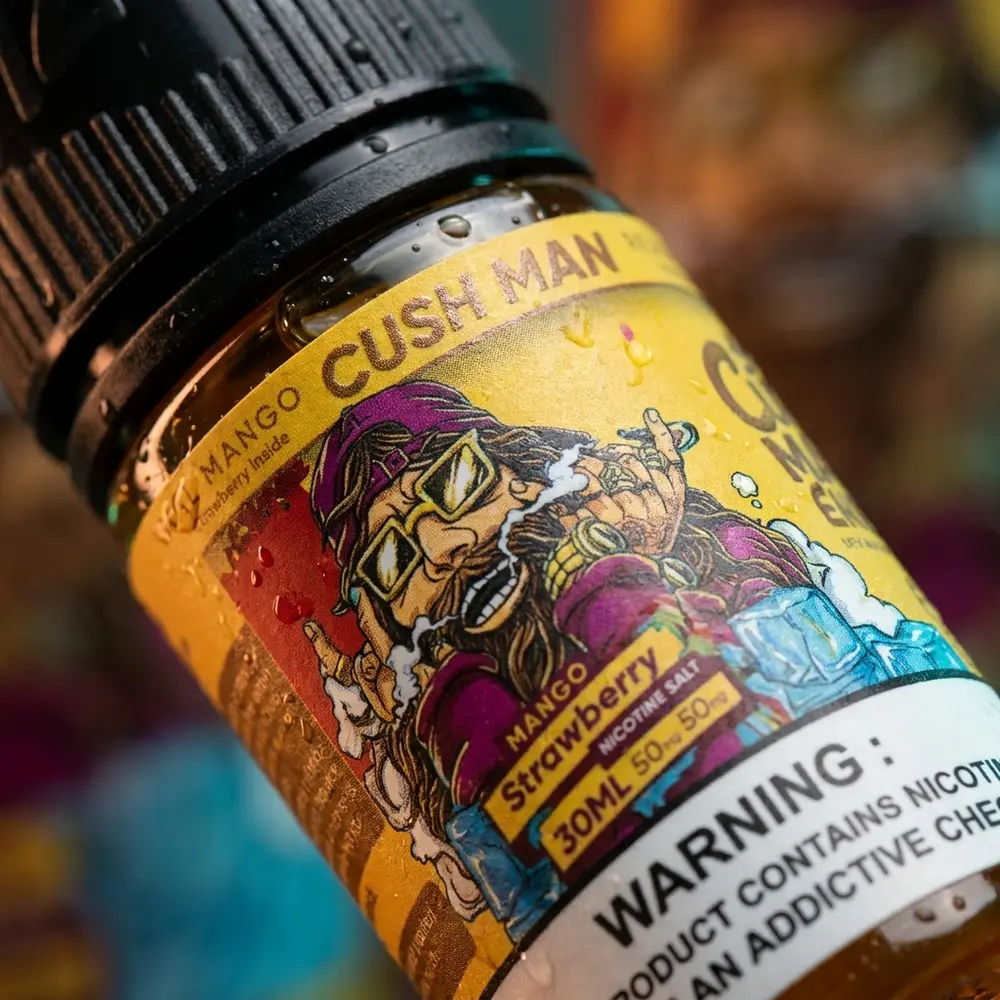 Detalhe macro do rótulo do Líquido Nasty Juice Salt Mango Strawberry com gotas, textura do vidro e reflexos - Vapor Gringo