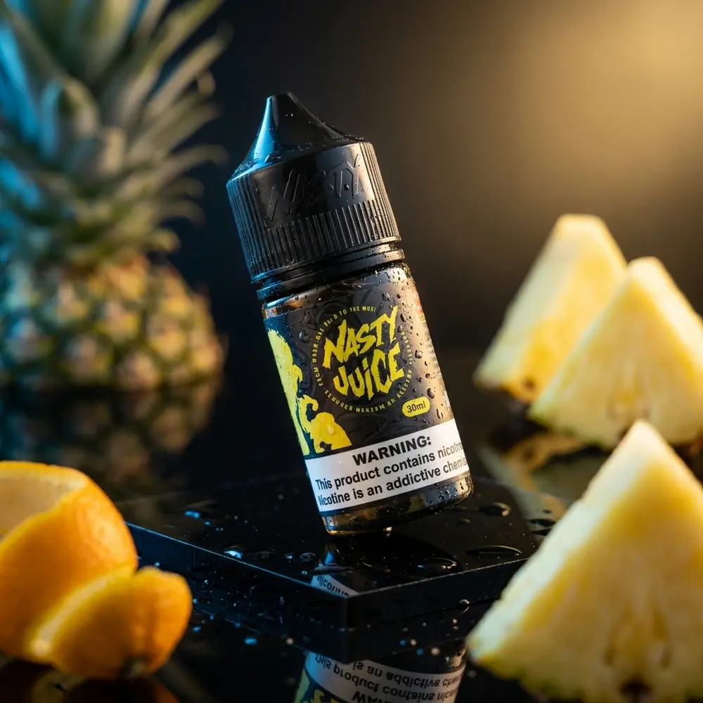 Líquido Nasty Juice Salt Pineapple sobre base acrílica preta, gotas e fatias de abacaxi ao fundo - Vapor Gringo